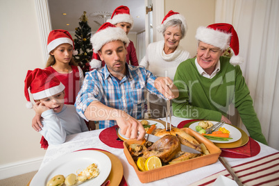 Father in santa hat carving chicken during dinner