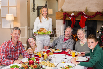 Woman holding turkey roast with family at dining table