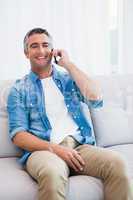 Smiling man sitting and phoning on the couch