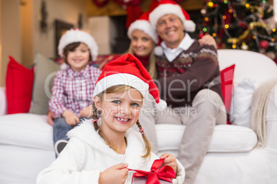 Smiling little girl opening a gift with her family behind