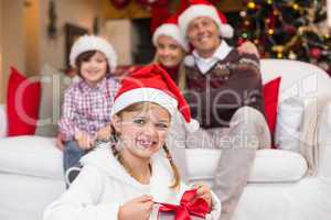 Smiling little girl opening a gift with her family behind