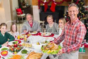 Man holding turkey roast with family at dining table