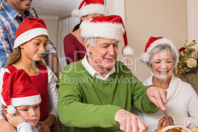 Grandfather in santa hat carving chicken at christmas dinner