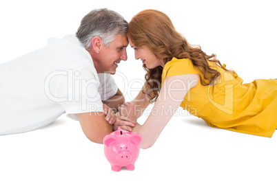 Casual couple lying on floor with piggy bank