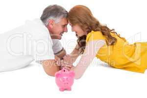 Casual couple lying on floor with piggy bank