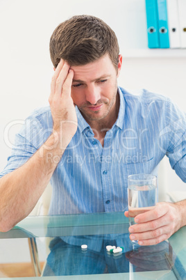 Hungover businessman holding glass of water and tablet