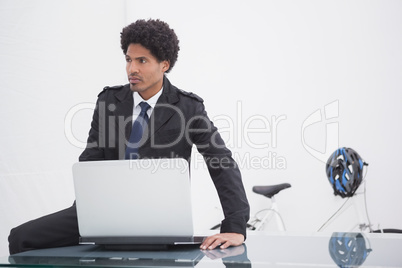 Thoughtful businessman in trench coat using laptop