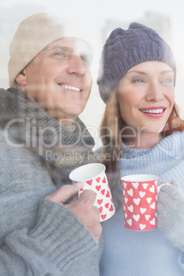 Happy couple in warm clothing holding mugs