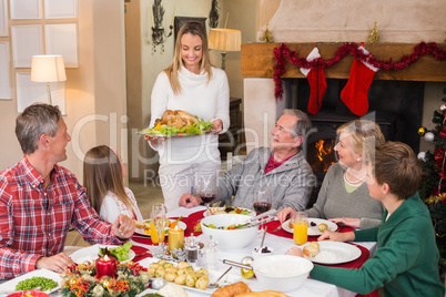 Woman holding turkey roast with family at dining table