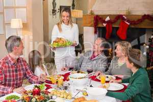 Woman holding turkey roast with family at dining table