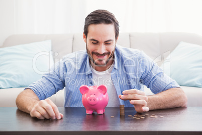 Smiling businessman putting coins into piggy bank