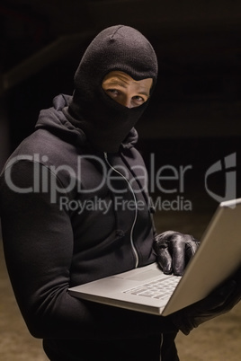 Burglar standing holding laptop while looking at camera