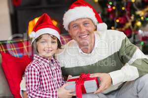 Son offering father a christmas gift on the couch