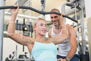 Male trainer assisting woman on a lat machine in gym