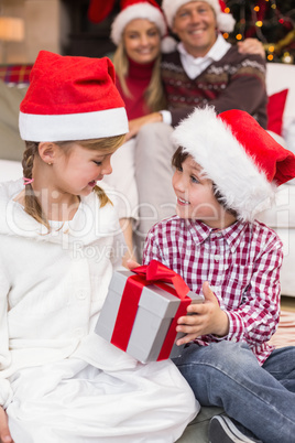 Festive little siblings opening a gift in front of their parents