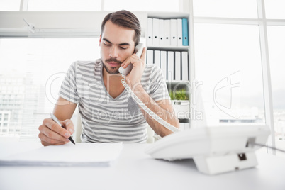 Casual businessman writing and phoning at his desk