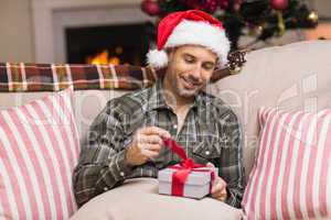 Smiling man in santa hat opening a gift