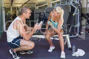 Male trainer assisting woman with dumbbell in gym