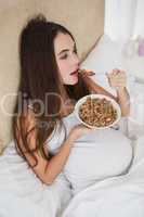 Pregnant brunette eating cereal in bed