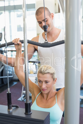 Male trainer assisting woman on lat machine in gym