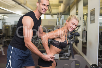 Male trainer assisting woman with dumbbell in gym