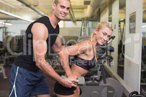 Male trainer assisting woman with dumbbell in gym