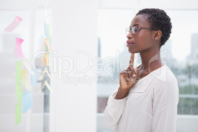 Thoughtful businesswoman looking at sticky notes on window