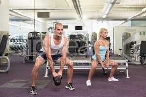 Fit couple lifting kettle bells in gym