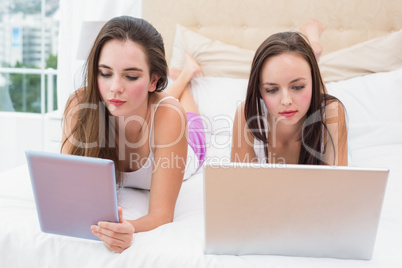 Pretty friends using their technology on bed
