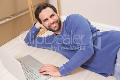 Happy man lying on floor using laptop