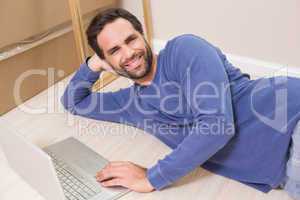 Happy man lying on floor using laptop