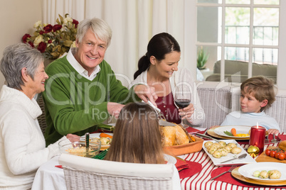 Happy grandfather carving chicken during christmas dinner