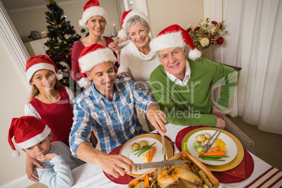 Father in santa hat carving chicken during christmas dinner