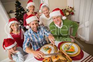 Father in santa hat carving chicken during christmas dinner