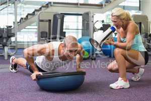 Trainer assisting man with push ups at gym