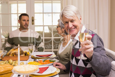 Smiling grandfather toasting at camera in front of his family