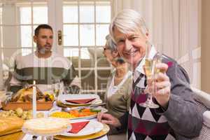 Smiling grandfather toasting at camera in front of his family
