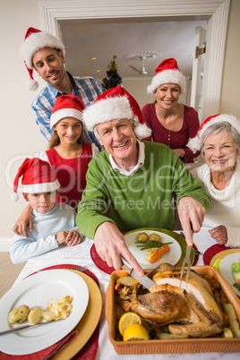 Grandfather in santa hat carving chicken at christmas dinner