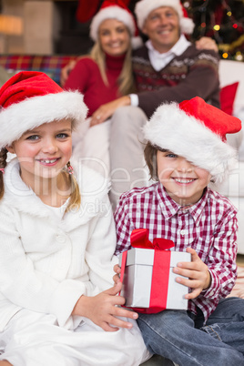 Festive little siblings opening a gift in front of their parents