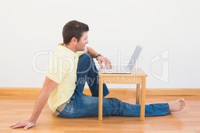 Casual man sitting on floor using laptop on the coffee table at