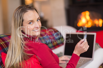 Smiling blonde shopping online with laptop at christmas