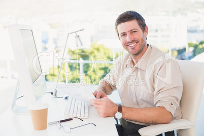 Smiling businessman looking at document at his desk