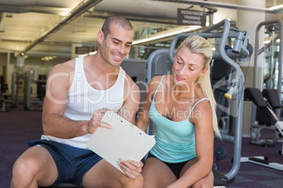 Woman discussing her performance on clipboard with trainer at gy