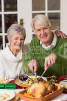 Man carving chicken while his wife having arm around him