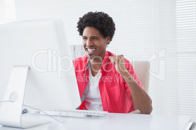 Smiling casual businessman cheering at his desk