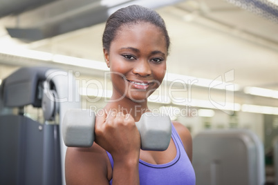 Fit woman smiling at camera holding dumbbell