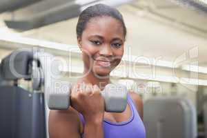 Fit woman smiling at camera holding dumbbell