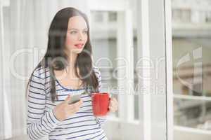 Pretty brunette holding mug and phone