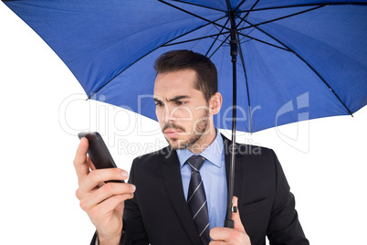 Concentrated businessman under umbrella using mobile