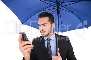 Concentrated businessman under umbrella using mobile